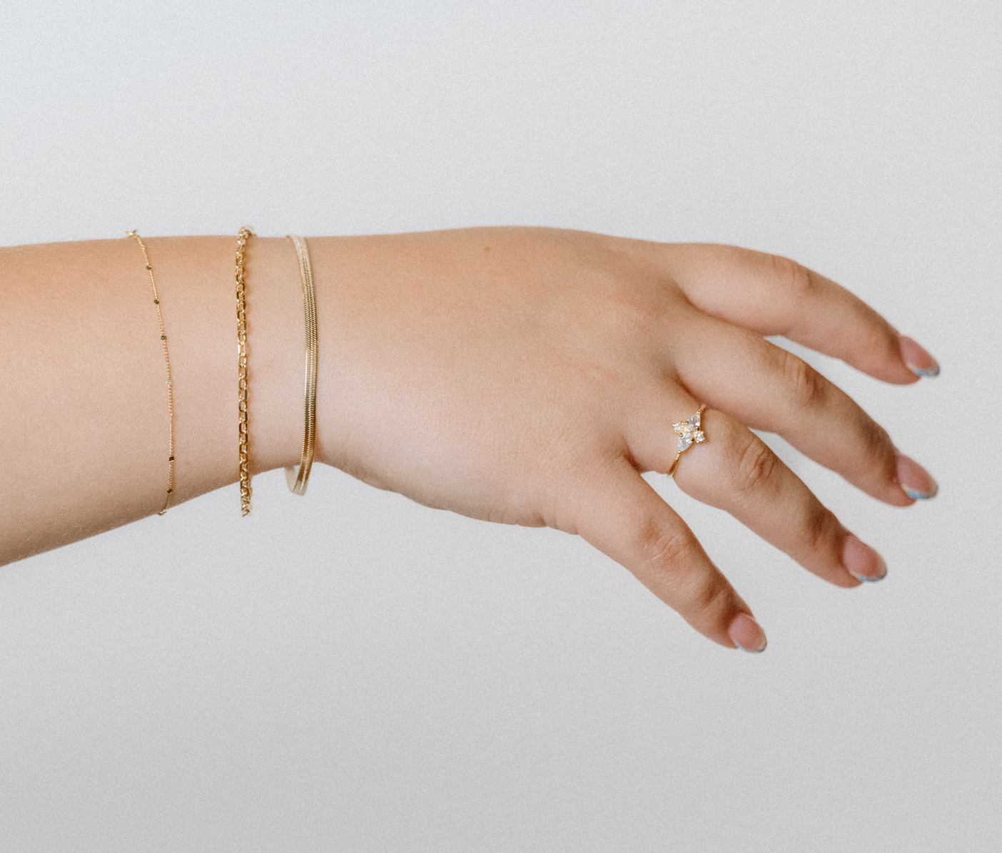 Outstretched hand wearing minimalist gold bracelets and a pavé butterfly ring against a neutral background.