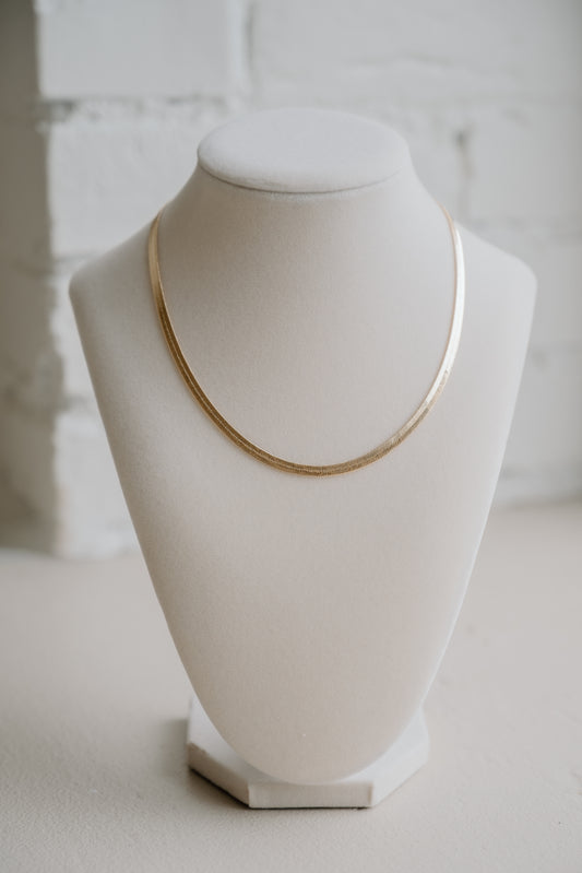 Gold necklace on a white mannequin bust against a light background
