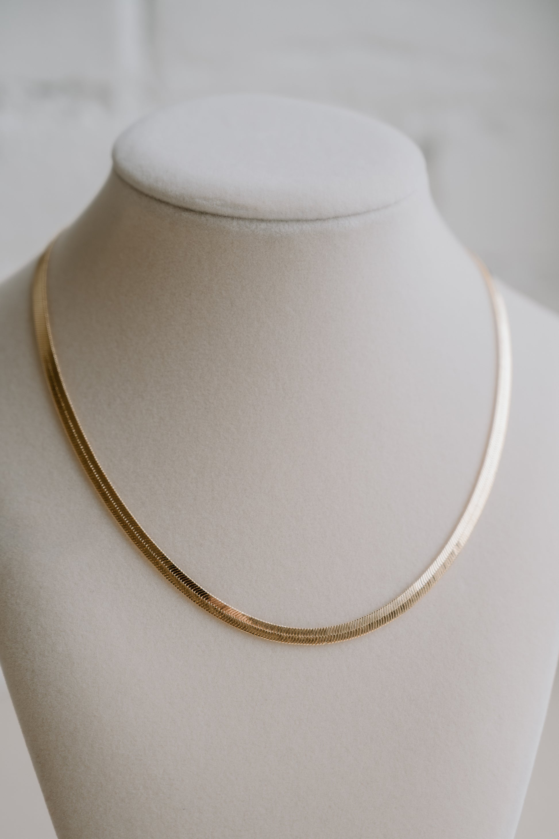 Gold necklace on a mannequin bust against a plain background